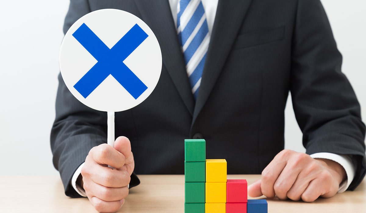 「バツ」の札を掲げるスーツの男性